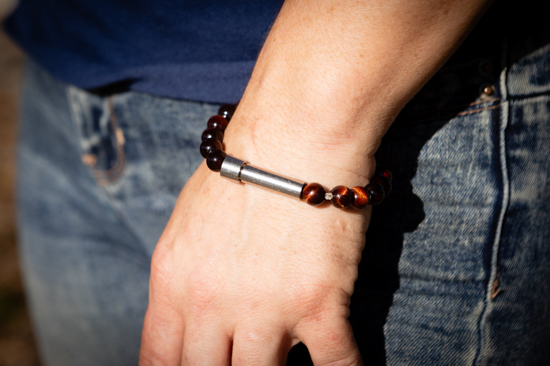 Hand wearing a cremation bracelet with beads, wearing blue jeans outdoors.