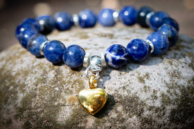 sodalite beaded urn bracelet with a gold heart charm on a stone surface