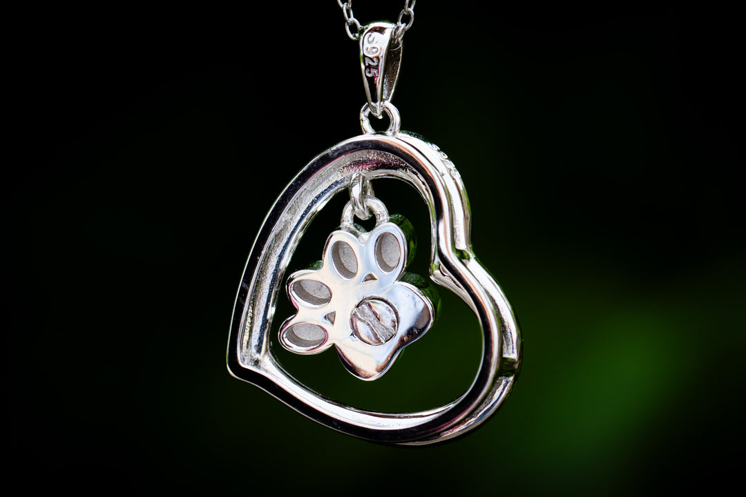 Close up of a sterling silver pawprint cremation pendant on a chain circular open frame with paw print centerpiece bail stamped 925