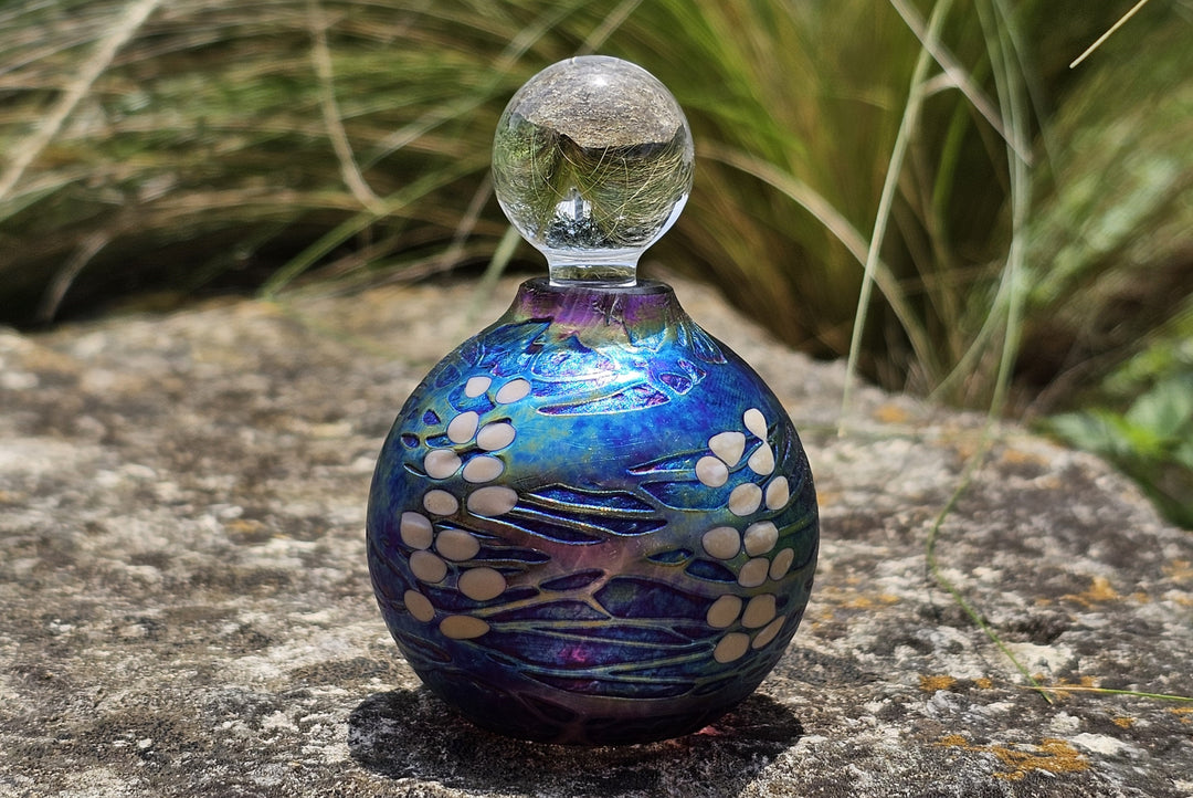 Blue and purple glass keepsake urn with a clear spherical stopper and white leaflike accents