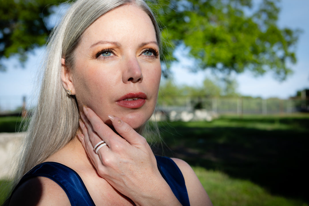 Woman with gray hair and blue eyes outdoors, wearing a hair keepsake ring on her finger.