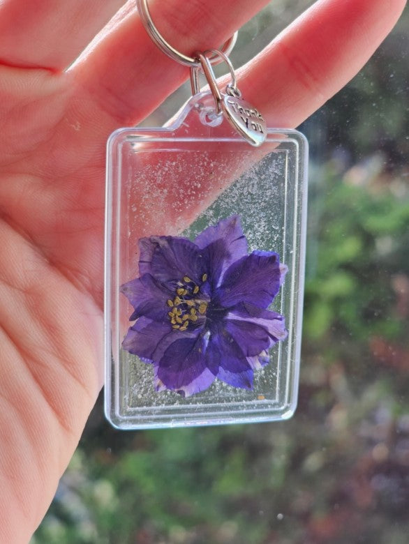 Single cremation ash flower keychain with a purple dried blossom inside a clear frame and a Thank You charm on the ring.