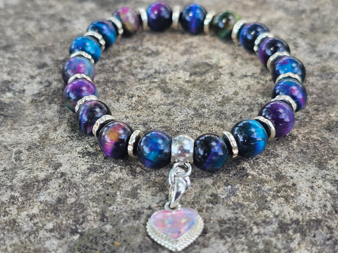 Rainbow Tiger Eye cremation bracelet with a silver heart charm and crushed opal in light pink and blue tones shown on a neutral background