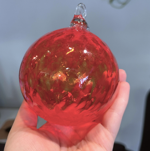 Red glass Christmas ornament infused with cremation ashes, shown being held in a hand.
