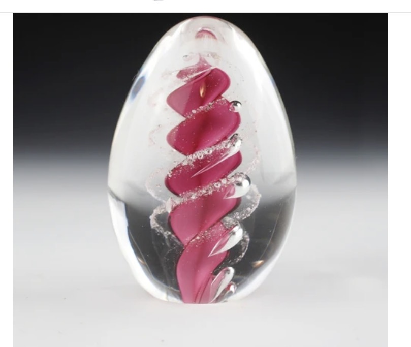 Clear glass paperweight with pink and white design on a gradient background