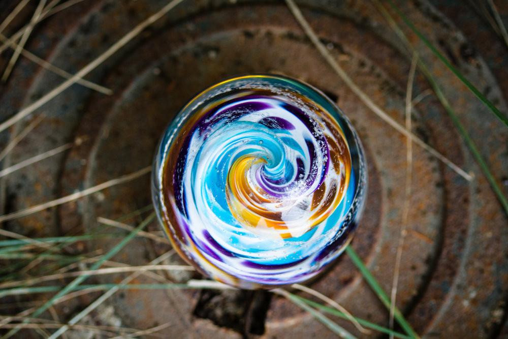 Top view of a colorful glass cremation orb with cremains, featuring blue yellow purple and green swirls