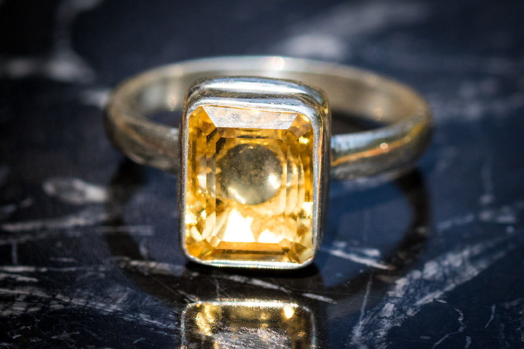 Front view of a yellow rectangular citrine ring in a bezel setting on a dark marble surface.