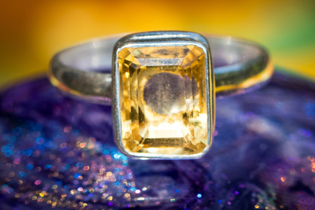 Close up of a yellow square-cut citrine gemstone set in a silver ring.
