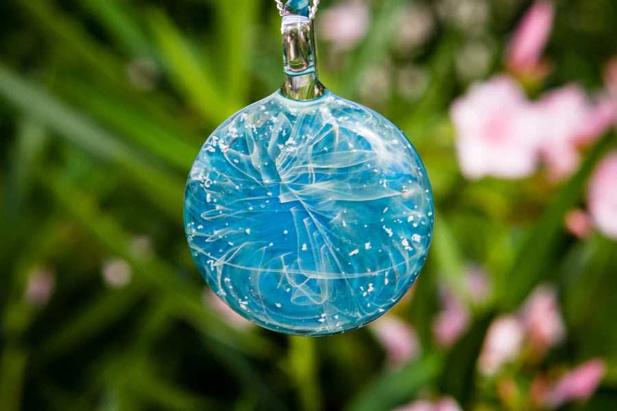 Turquoise glass pendant with embedded cremation ashes hanging from a dark cord necklace.