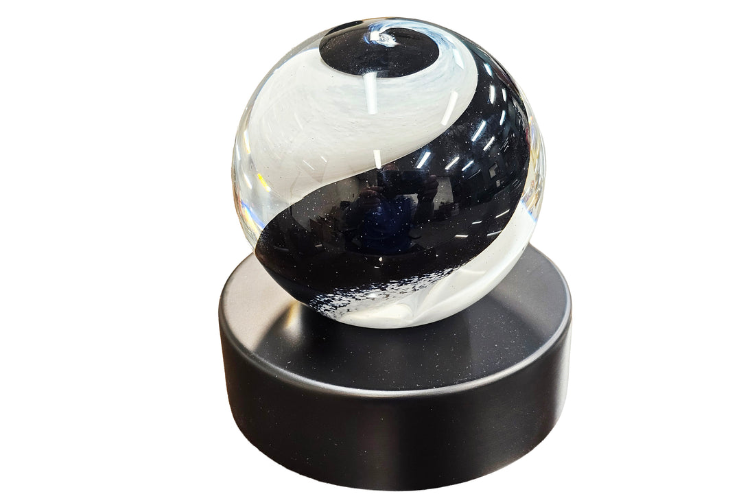 glass ball with black and white design on a black urn base against a white background for cremation ash