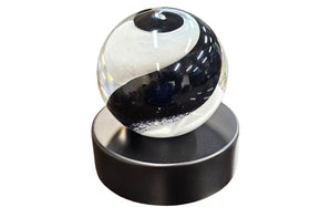 glass ball with black and white design on a black urn base against a white background for cremation ash