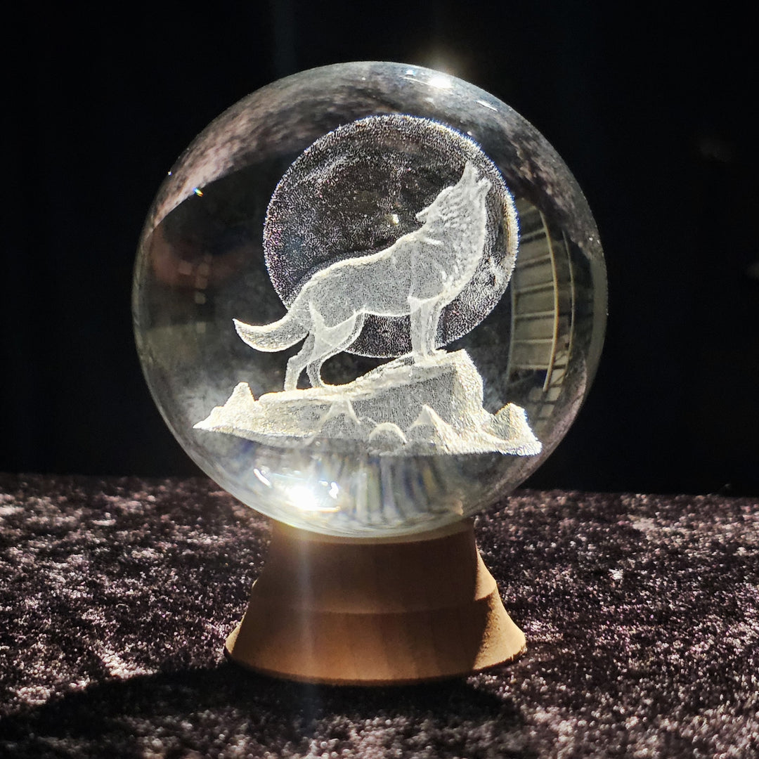 Crystal sphere featuring a howling wolf on a rocky ledge beneath a full moon on a wood stand