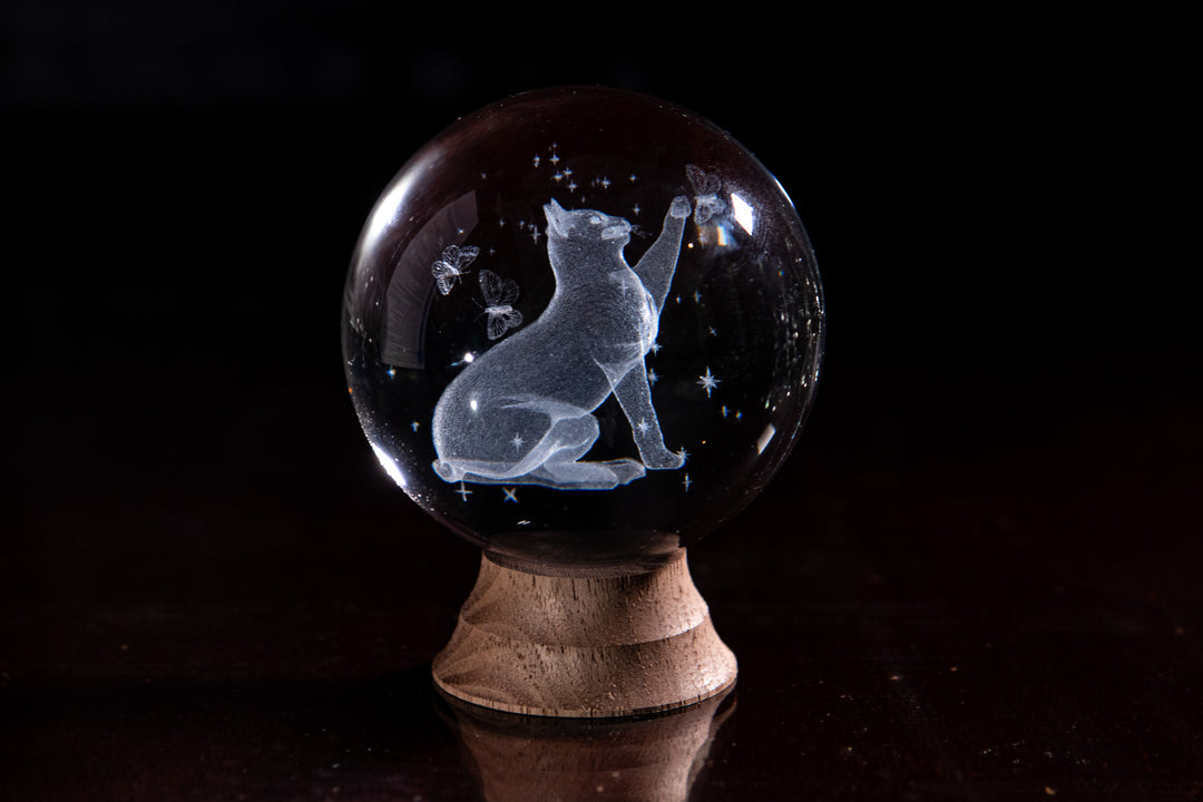 Clear crystal marble featuring a cat sitting and gazing with stars around it on a wooden stand.