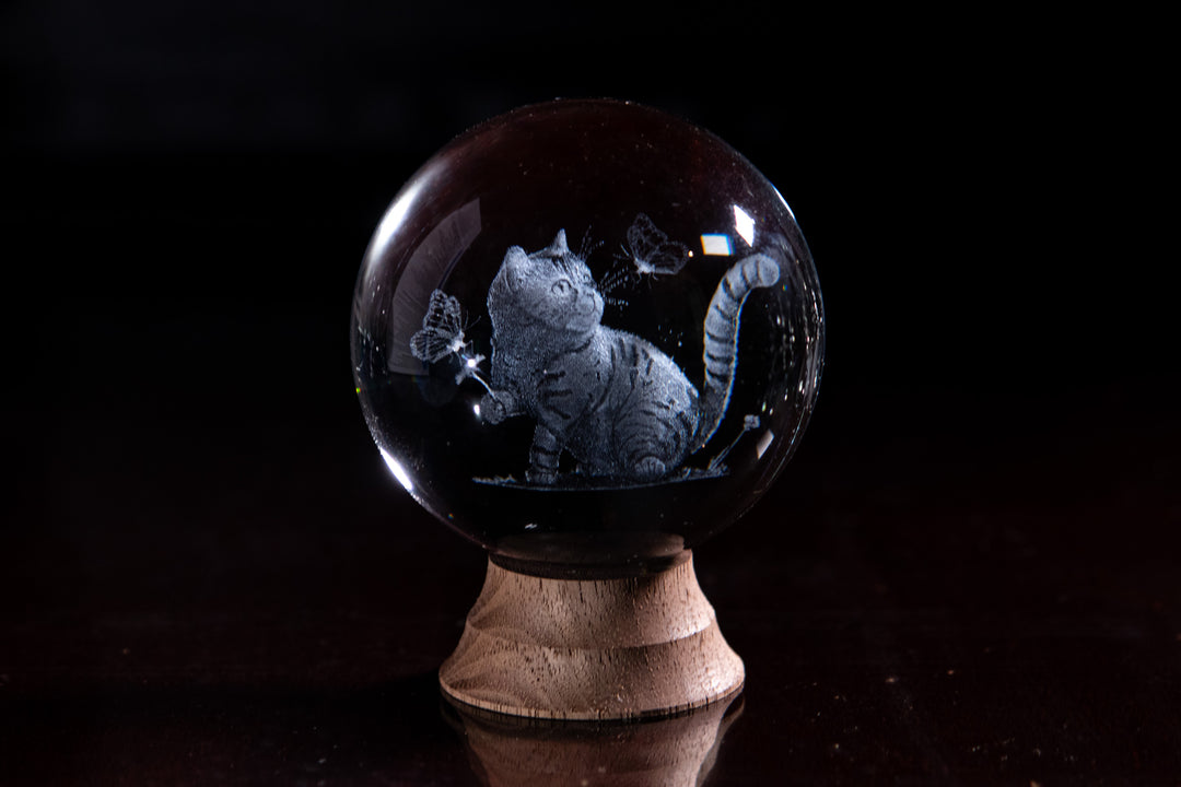 Clear crystal marble with a cat sitting and reaching toward butterflies, on a wooden stand.