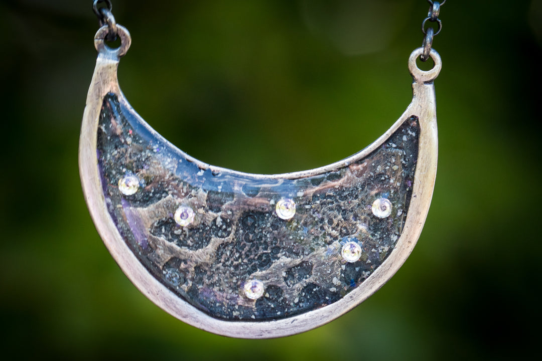 Crescent moon pendant with blue resin inlay and embedded crystals set in a silver border with chain.
