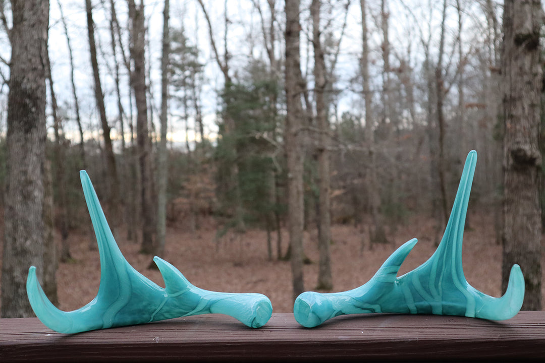 Pair of turquoise deer antler sculptures infused with cremation ash on a wooden deck with forest backdrop