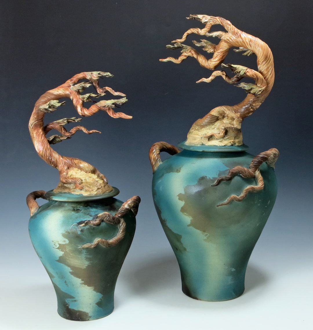 Cyprus Ginger memorial urns for ashes in two sizes with copper twisted tree finials atop teal glazed vases.