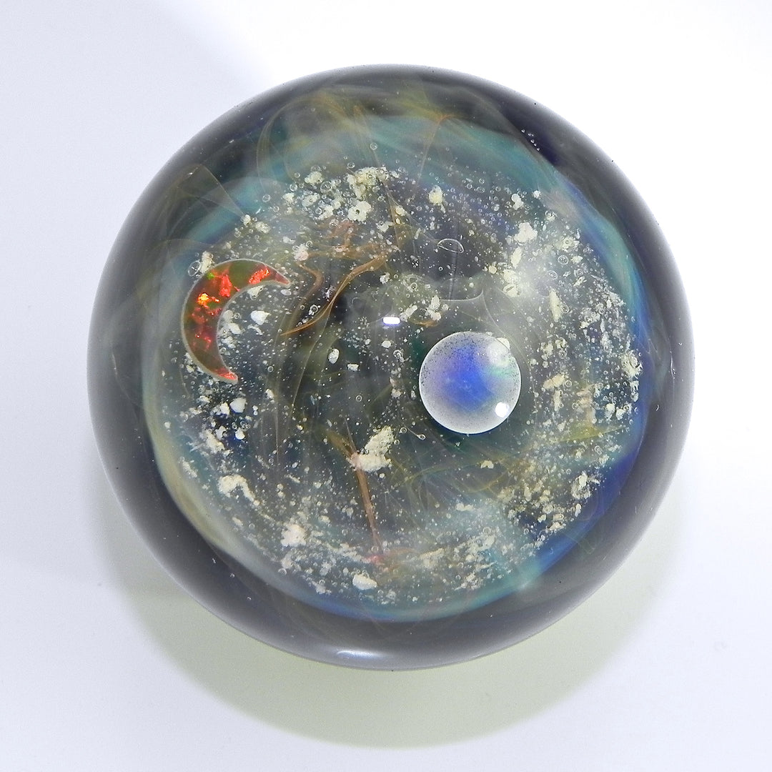 Wave Galaxy Marble with cremains featuring a starry half with two opals and a dichroic wave half inside a dark glass orb with silver specks