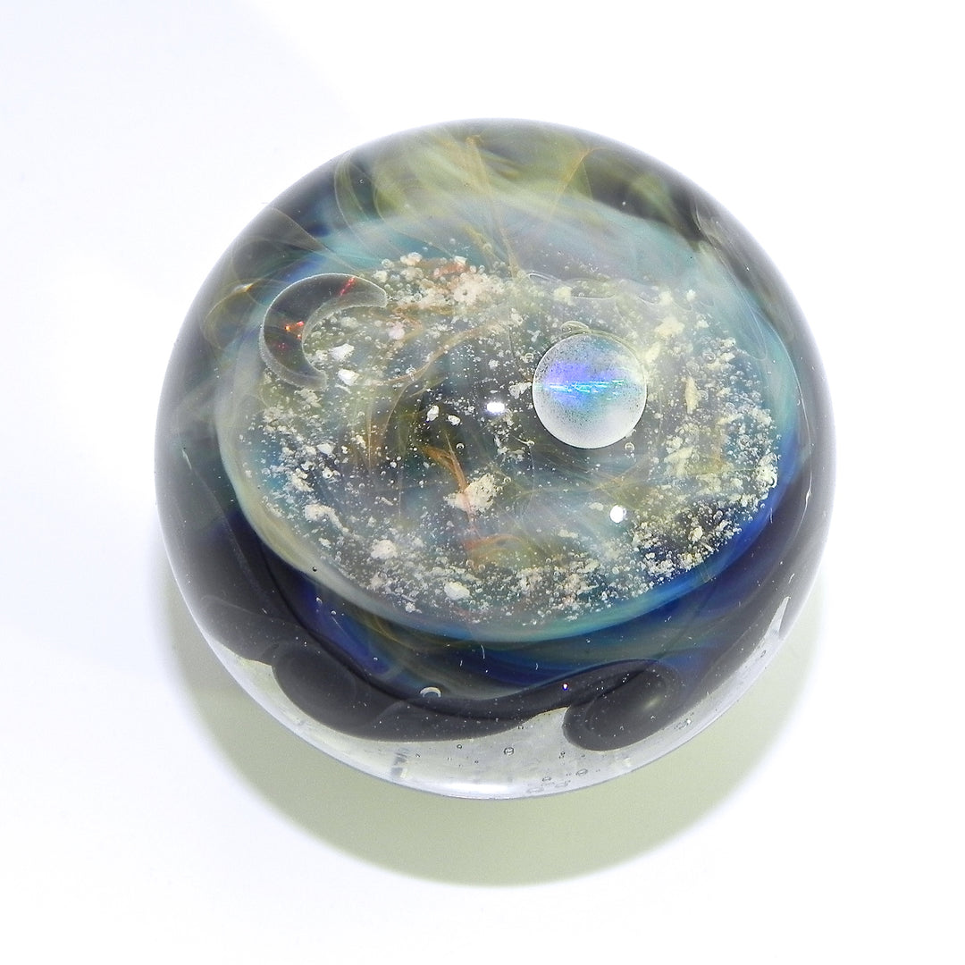 Wave Galaxy Marble with cremains showing a white orb, amber swirls, and scattered particles inside a clear sphere