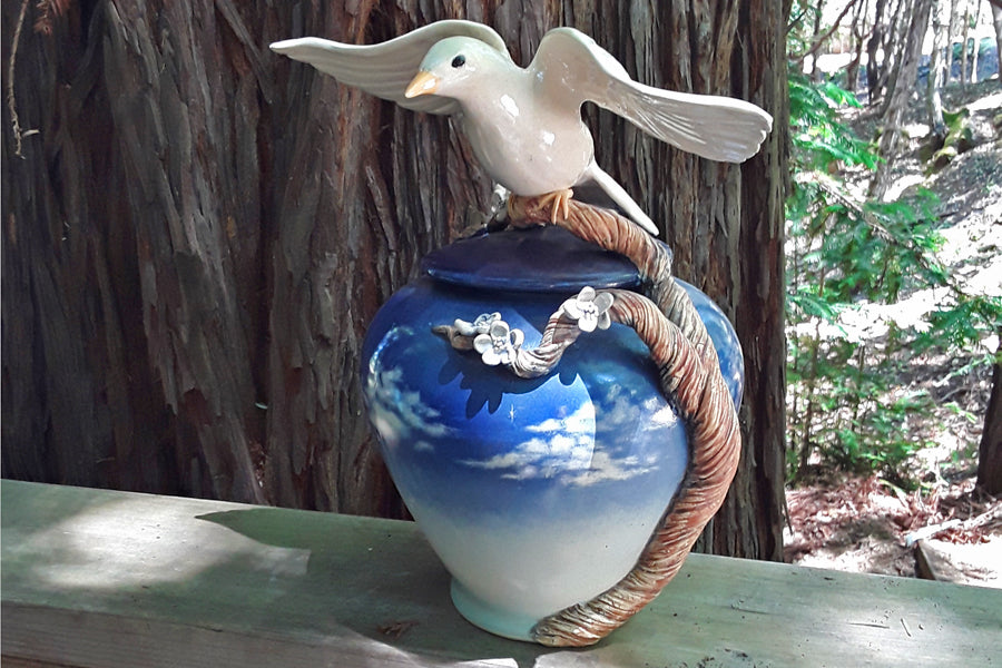 Handmade ceramic urn with a white dove perched on a twisting branch over a blue gradient vase