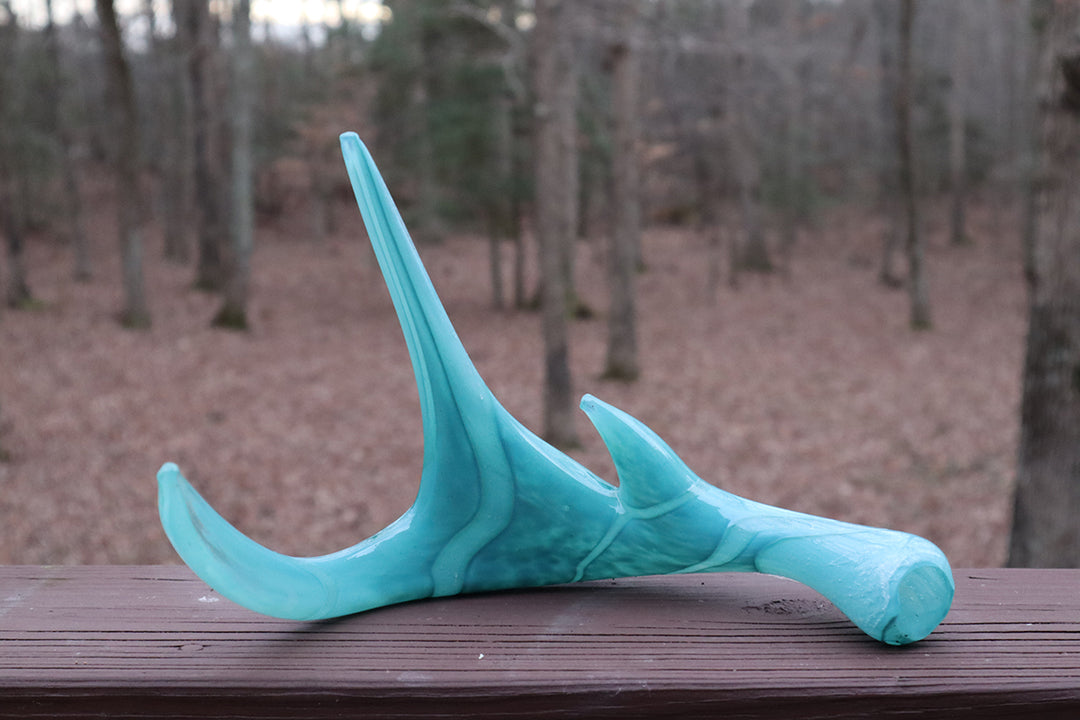 Turquoise deer antler sculpture infused with cremation ash rests on a wooden deck outdoors