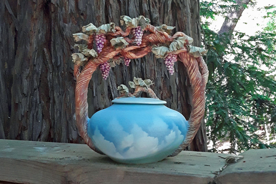 Blue ceramic urn with a grapevine arch and grape clusters adorning the handles.