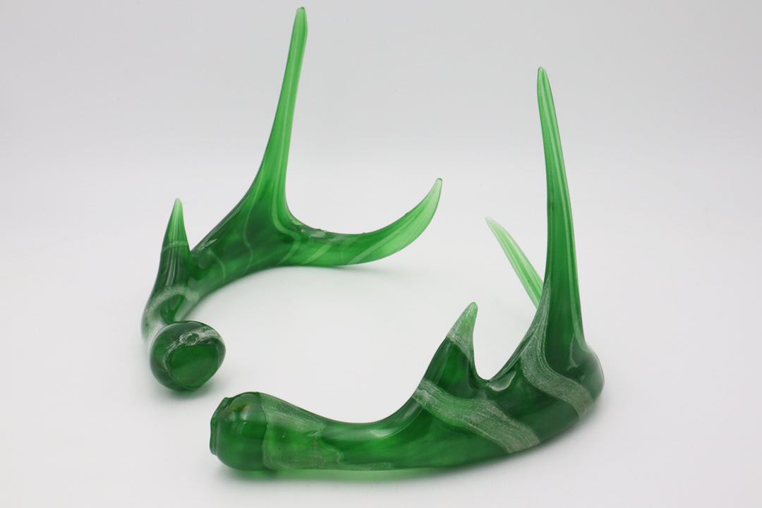 Close up of curved translucent green glass deer antlers against a light background