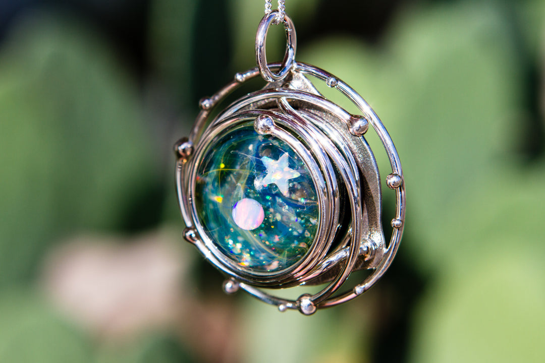 Model wearing the galaxy pendant on a silver chain against a blurred green background