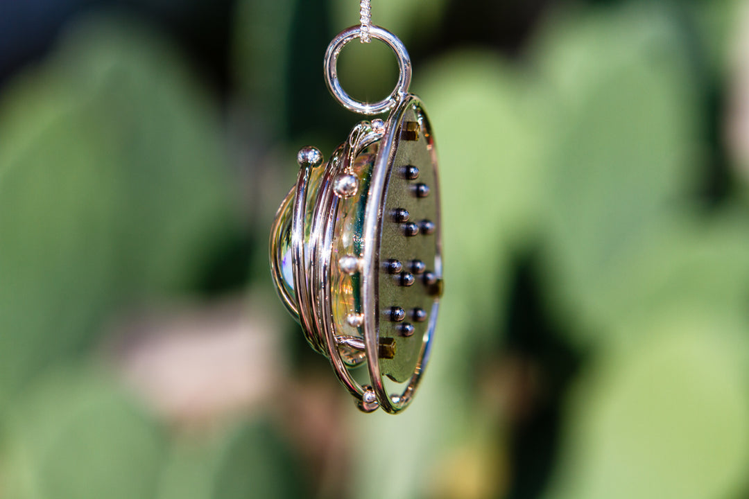 Side view of a silver circular cage necklace around a blue galaxy glass cabochon