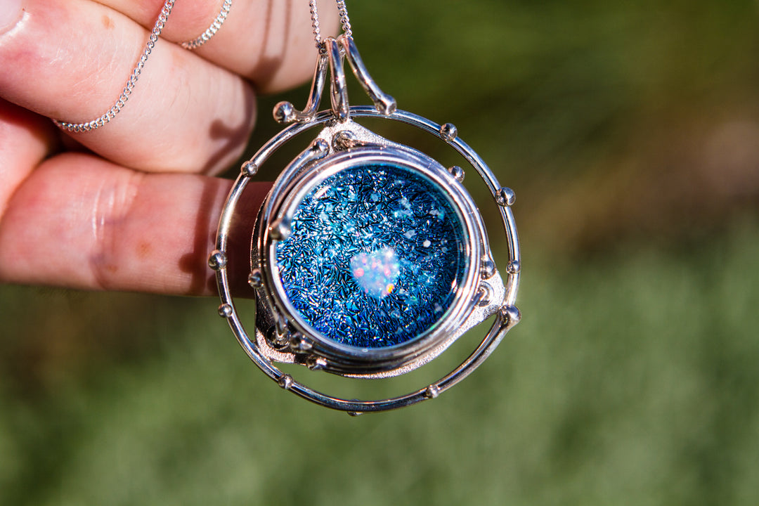 Front view of the Caged Heart in Stars pendant showing a blue galaxy cabochon with a pink heart inside a silver cage