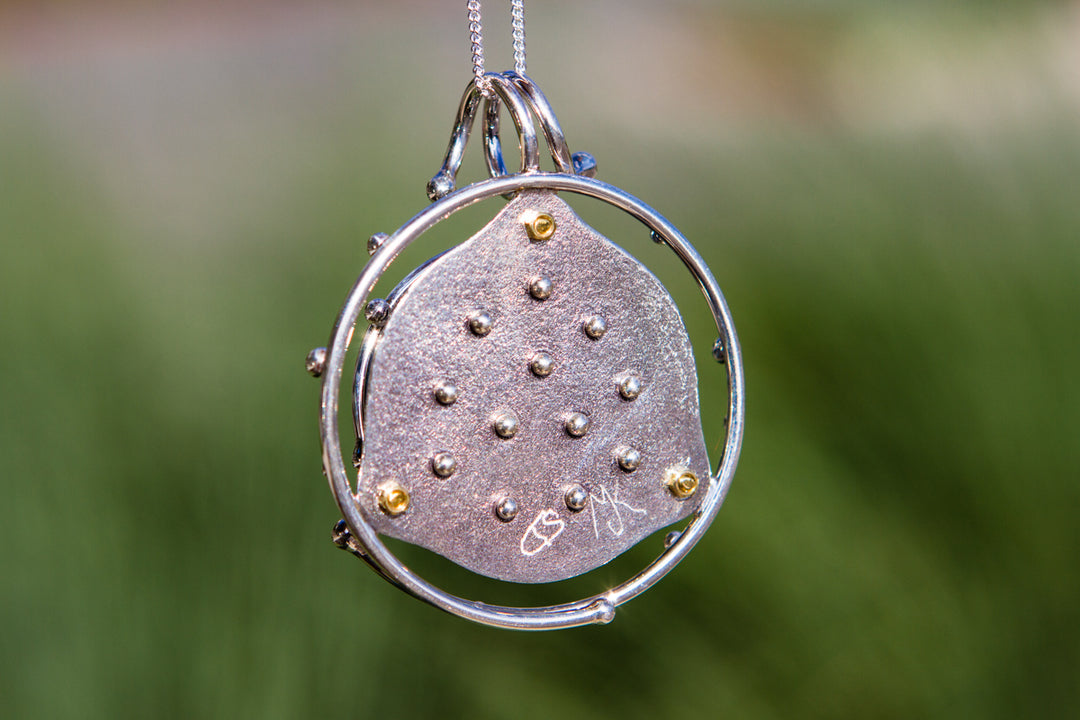 Round silver cage pendant with a glass galaxy cabochon inside attached to a chain