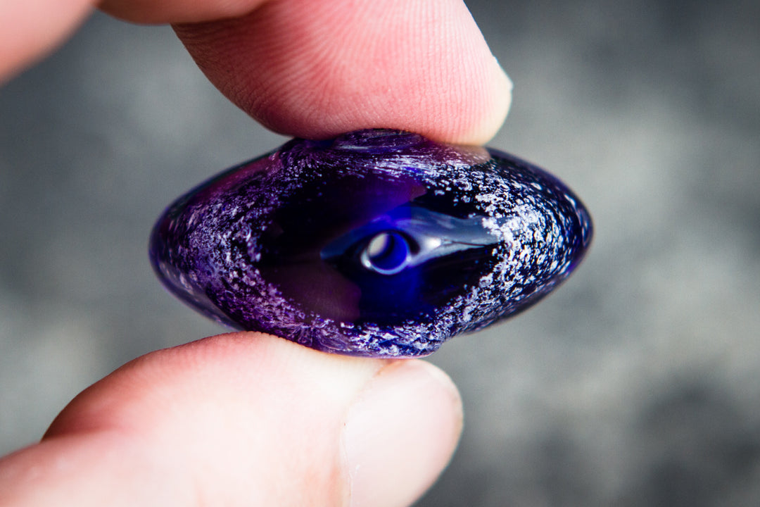 Purple glass cremation ash pendant cabochon with a predrilled hole held between fingertips