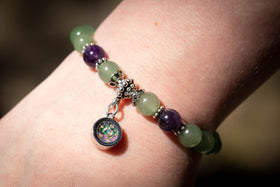 Photo depicts the aventurine and amethyst bracelet on a model's wrist. The dainty circle charm, made with green and dusk blue opal, faces towards the viewer. Aventurine bracelet, aventurine jewelry, amethyst bracelet, amethyst jewelry, natural stone jewelry, remembrance jewelry, jewelry for cremation ash, bracelet for ash