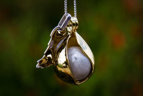 Close up of gold plated Angel Tear pendant with wing and glass marble inside against a green background