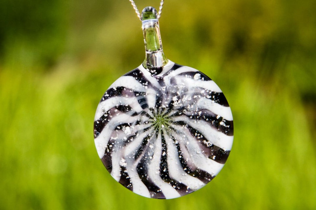 Black and white circular glass pendant with a starburst swirl and ash specks on a silver chain.
