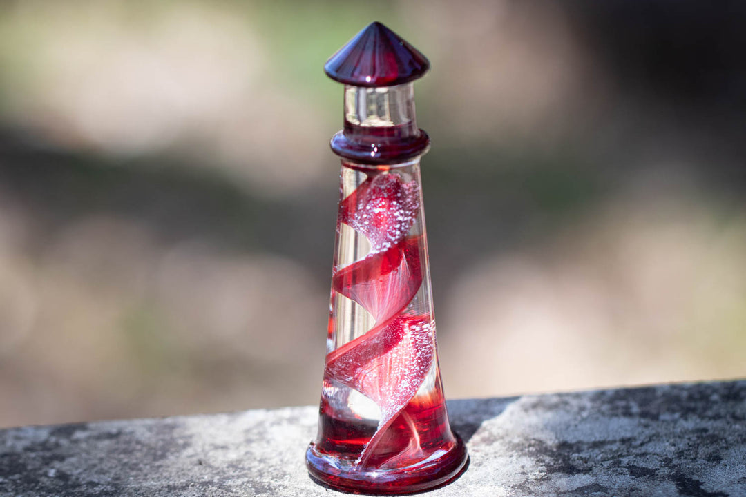 Red spiral memorial glass lighthouse with purple cap on a weathered stone surface.