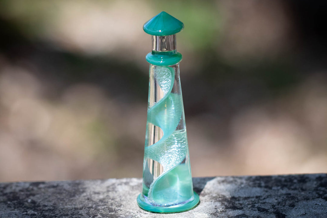 Giant memorial glass lighthouse infused with cremains, turquoise spiral inside and teal cap on a stone surface
