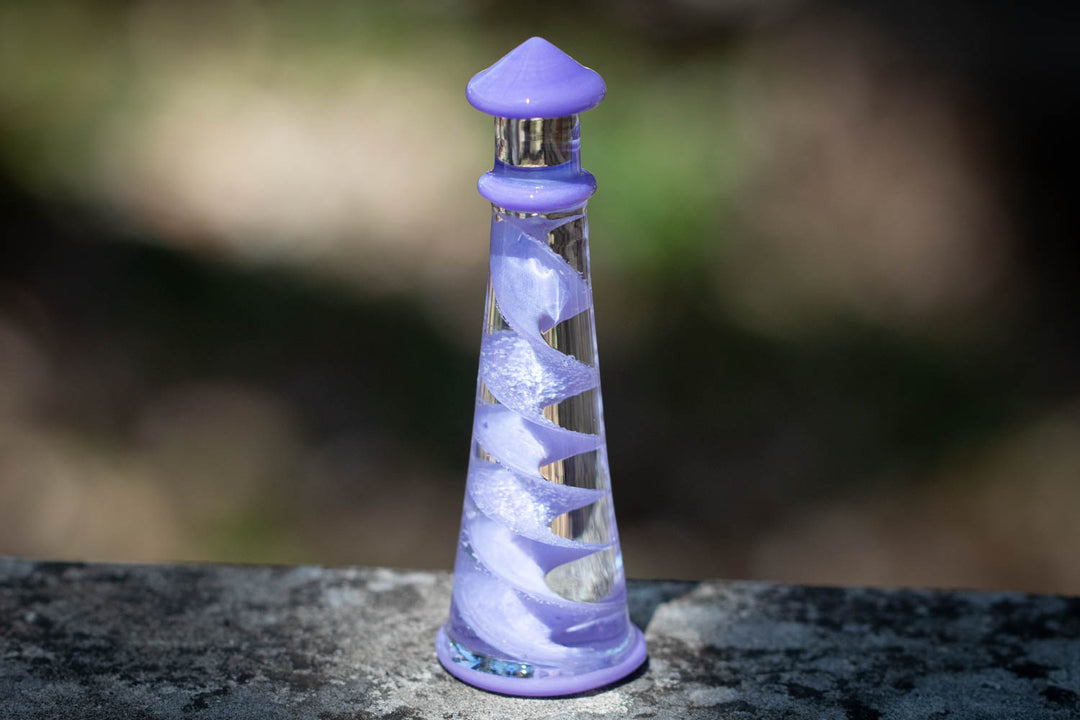 Giant memorial glass lighthouse infused with cremains, purple spiral inside and purple cap on a stone surface