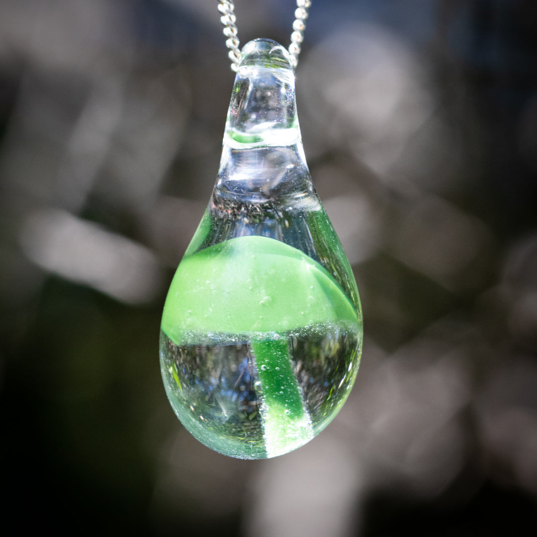 Mushroom pendant infused with cremation ash, a green mushroom encased in clear glass suspended from a cord necklace.