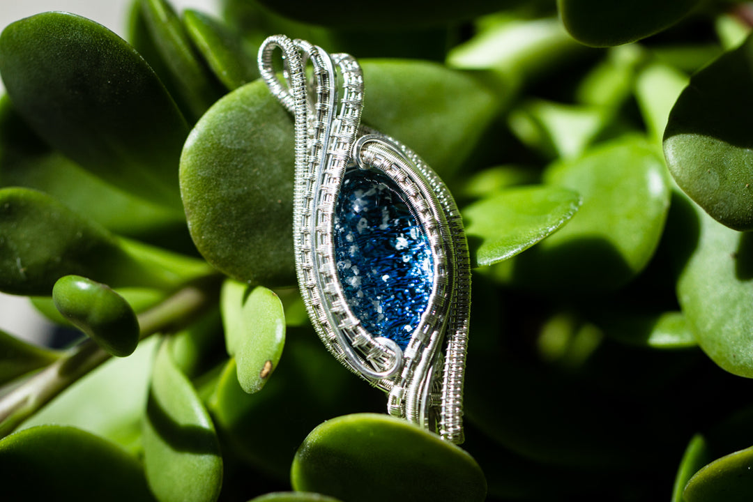 Madison wire wrapped pendant with a blue infused cabochon, intricate silver wire wrapping, shown beside a quarter on a colorful background.