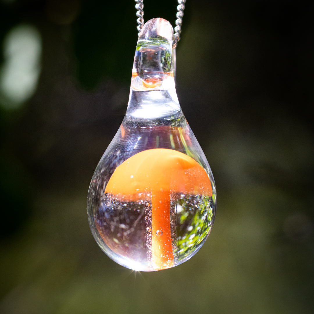 Clear glass teardrop pendant with an orange mushroom encased inside, suspended from a silver chain.