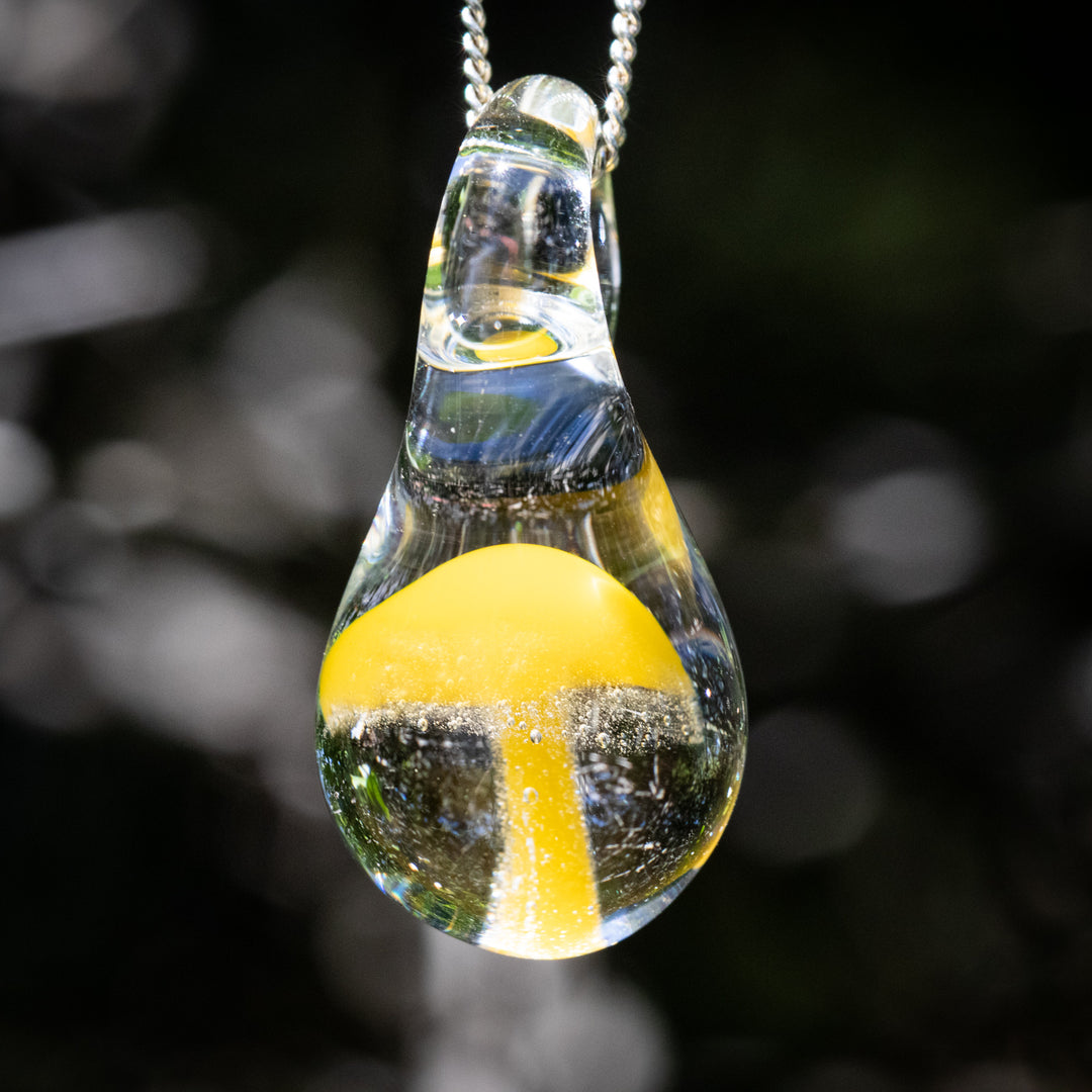 Clear glass teardrop pendant containing a bright yellow mushroom, hung from a silver chain.