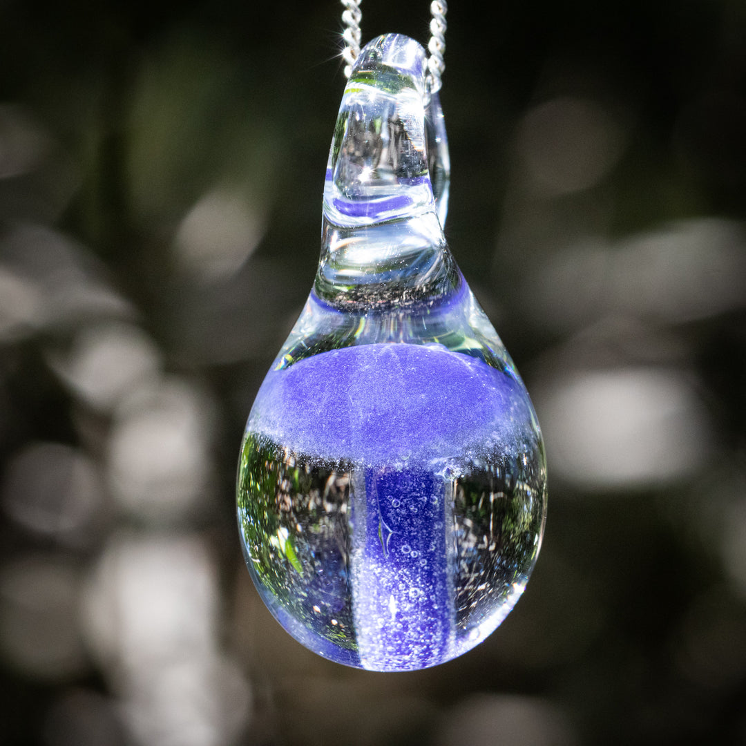 Blue mushroom encased in a clear borosilicate glass teardrop pendant on an adjustable silver cord infused with cremation ash