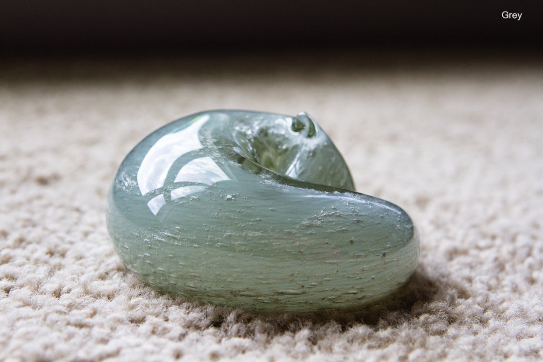 Sleeping grey glass cat paperweight with cremains visible beneath clear surface on carpet