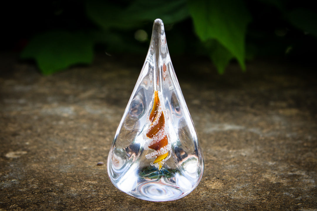 Clear teardrop glass memorial flame with orange and yellow cremation ash spiral inside