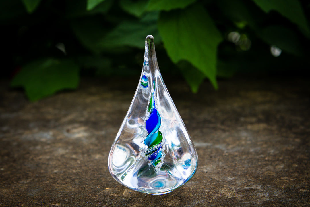 Clear glass pyramid flame with a blue and green spiral cremation ash encased inside.