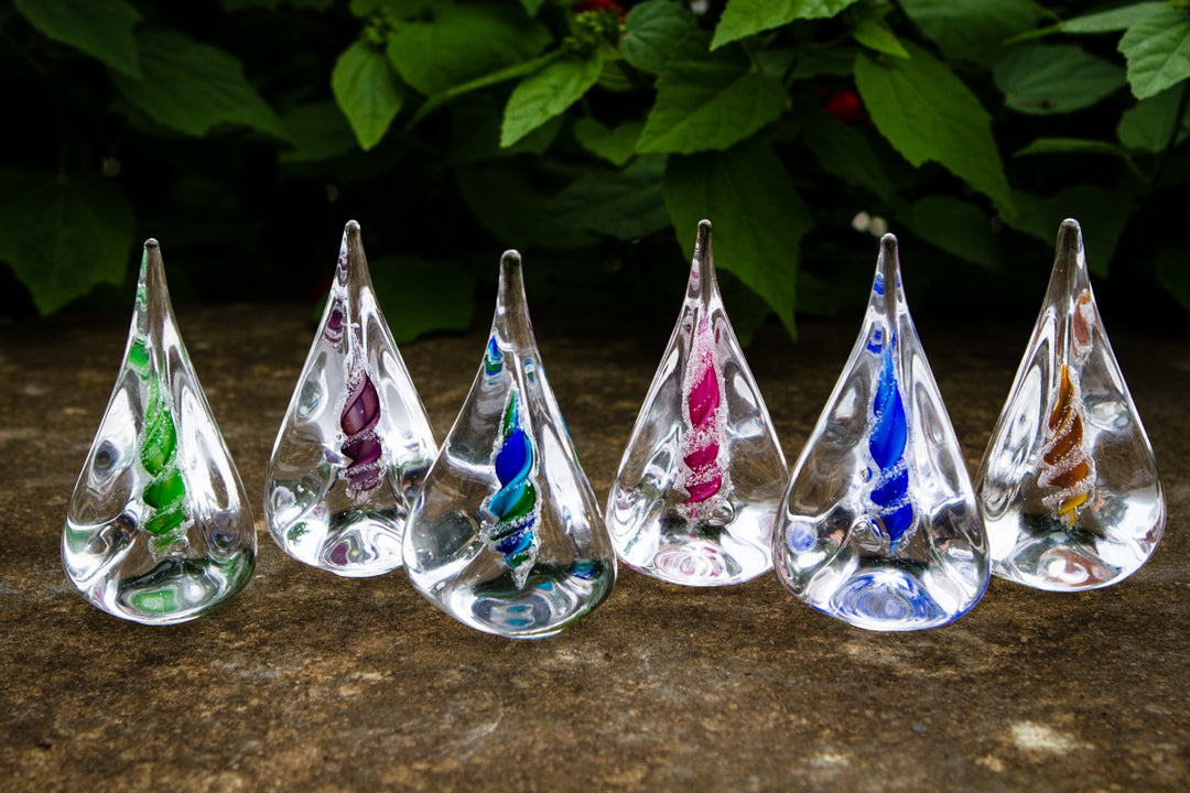 Clear glass memorial flame shapes with spiraled colorful interiors infused with cremation ash arranged in a row on a stone surface