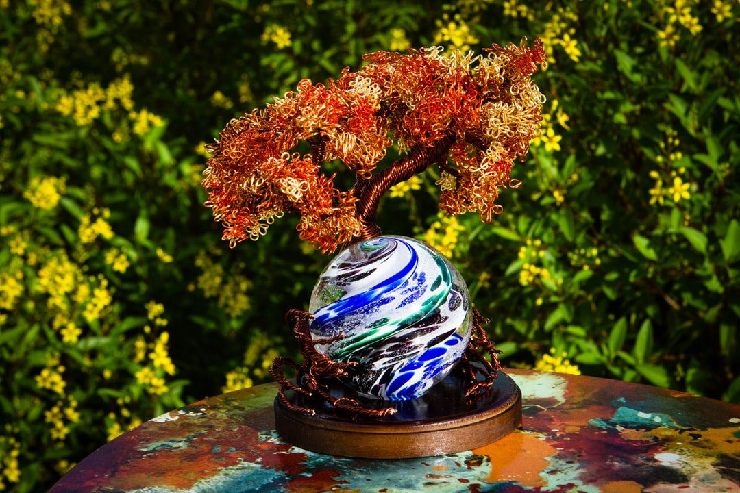 Autumn copper wire tree with orange leaves surrounding a blue and white marbled glass orb on a wooden stand.