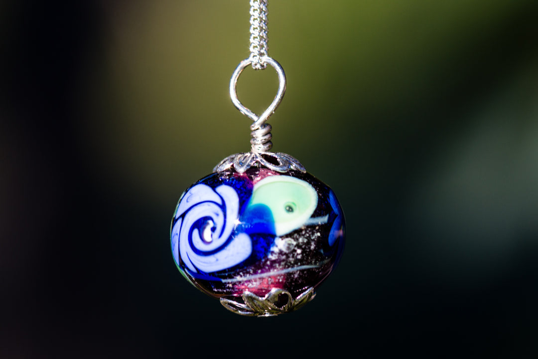Purple glass flower pendant with blue and white swirl patterns on a silver chain