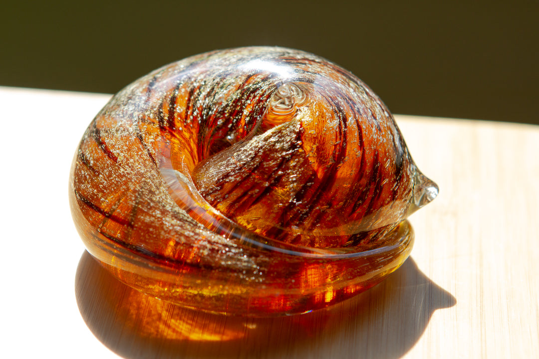 Amber orange glass sculpture with swirled textures on a wooden surface